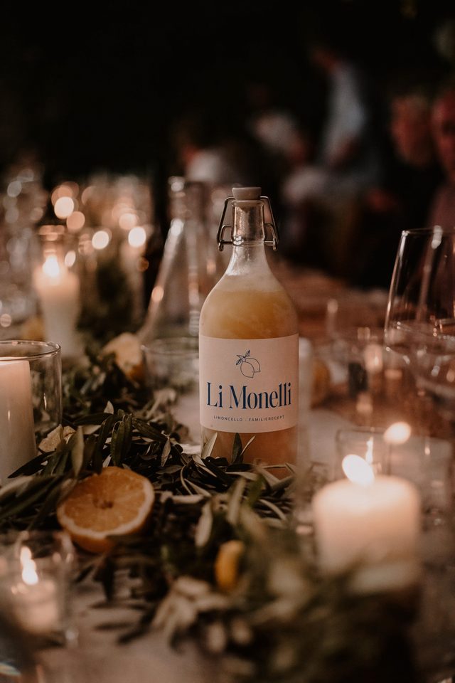 Fles Li Monelli limoncello tussen kaarsen, citroenen en olijftakken op een lange feesttafel in Italië